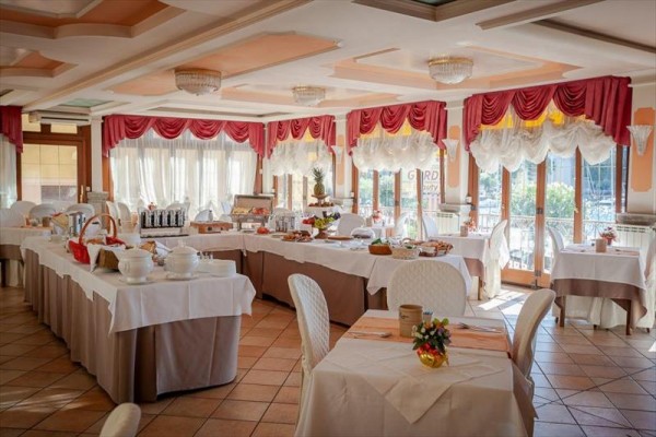Elegancka hotelowa jadalnia z przygotowanym stołem bufetowym i nakrytymi stolikami.