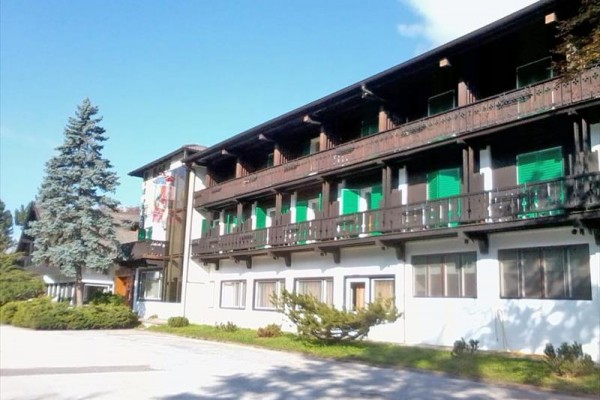 Budynek hotelowy z balkonami i zielonymi okiennicami obok niebieskiego drzewa.