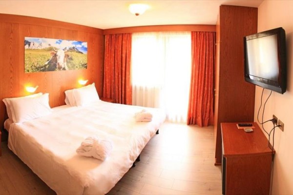 Jasny pokój hotelowy z łóżkiem małżeńskim, obrazem na ścianie i telewizorem na ścianie.
