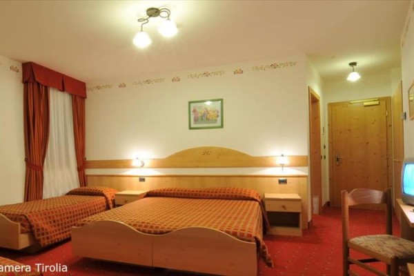 Pokój hotelowy z dwoma łóżkami, telewizorem i drewnianymi meblami w ciepłych kolorach.