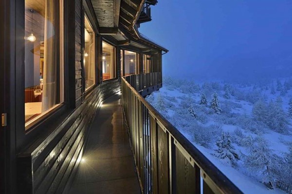 Wąski drewniany balkon obok oświetlonej restauracji z widokiem na ośnieżony krajobraz wieczorem.