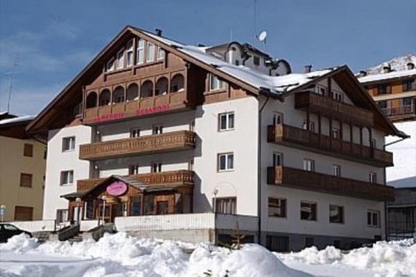 Alpejski zaśnieżony hotel z drewnianymi balkonami pod błękitnym niebem.