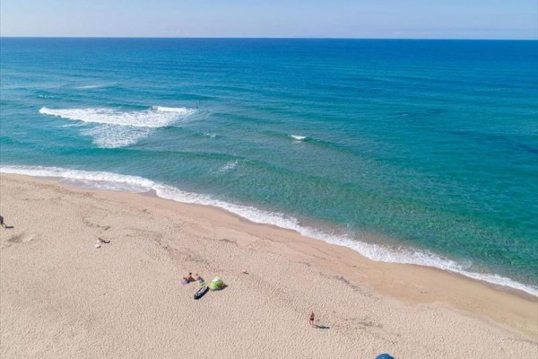 Piaszczysta plaża z kilkoma osobami nad niebieskim morzem.