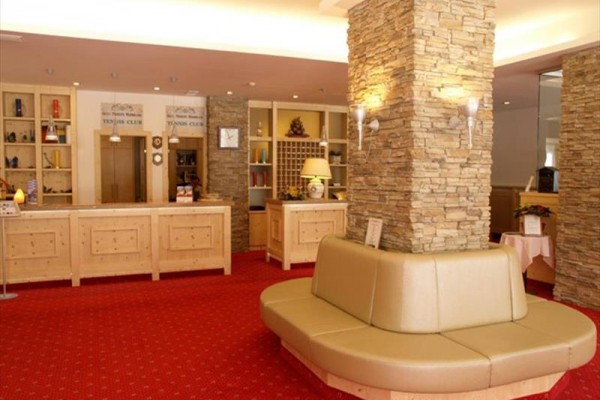 Hotelowa recepcja z czerwonym dywanem, kamiennymi kolumnami i drewnianymi meblami.  