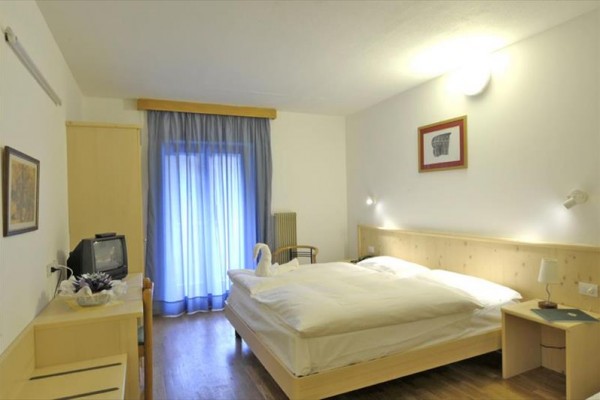 Jasny pokój hotelowy z łóżkiem małżeńskim, telewizorem i drzwiami balkonowymi.