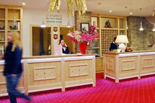 Recepcja hotelowa z pracownikami za ladą i kobietą przechodzącą obok.