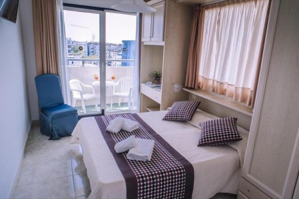 Mały pokój hotelowy z podwójnym łóżkiem i balkonem z widokiem na miasto.