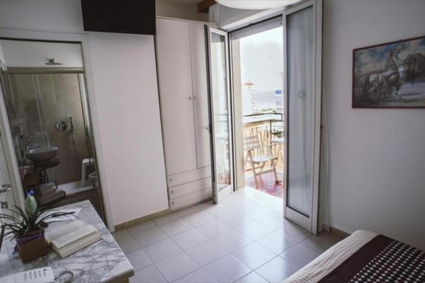 Pokój z otwartymi drzwiami balkonowymi prowadzącymi na balkon z widokiem na morze.