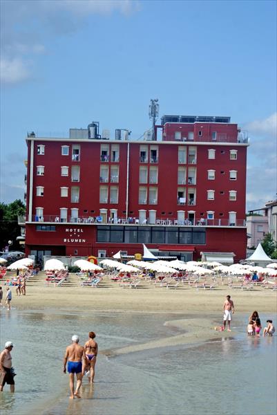 Hotel przy plaży z ludźmi spacerującymi po płytkiej wodzie.