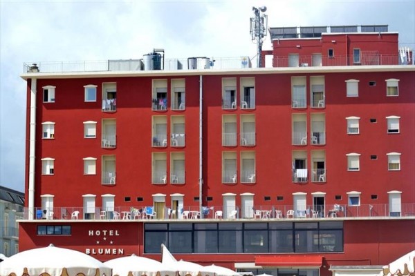 Ceglano-czerwona fasada hotelu z balkonami i zewnętrznymi miejscami do siedzenia.