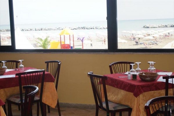 Restauracja z widokiem na plażę z kamiennym falochronem i parasolami.