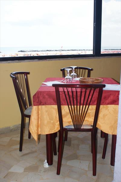 Przeszklona restauracja z widokiem na morze i stół z czterema krzesłami przykryty obrusem.