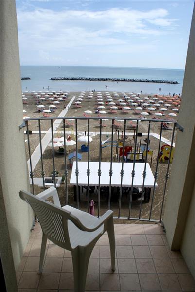 Widok z balkonu z plastikowym krzesłem na plażę z morzem i parasolami.
