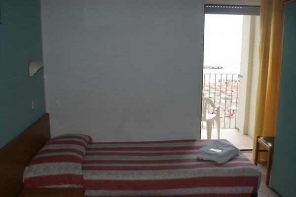 Pokój z wąskim łóżkiem i widokiem na balkon w stronę plaży.