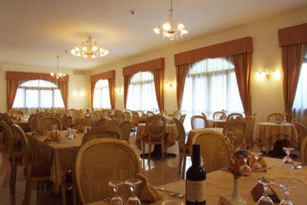 Przestronna restauracja z okrągłymi stołami i drewnianymi krzesłami pod eleganckimi żyrandolami.