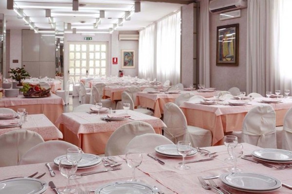 Elegancka restauracja z różowo nakrytymi stołami i białymi pokrowcami na krzesłach.