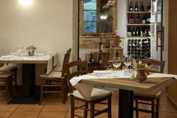 Restauracja z drewnianymi stołami, krzesłami i dekoracją zawierającą butelki wina na półkach.
