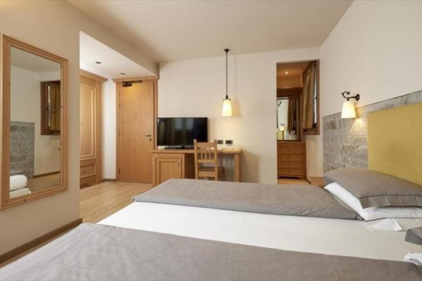 Nowoczesny pokój hotelowy z podwójnym łóżkiem, telewizorem i lustrem na ścianie.