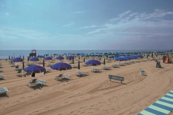 Piaszczysta plaża z niebieskimi parasolami i leżakami nad morzem.