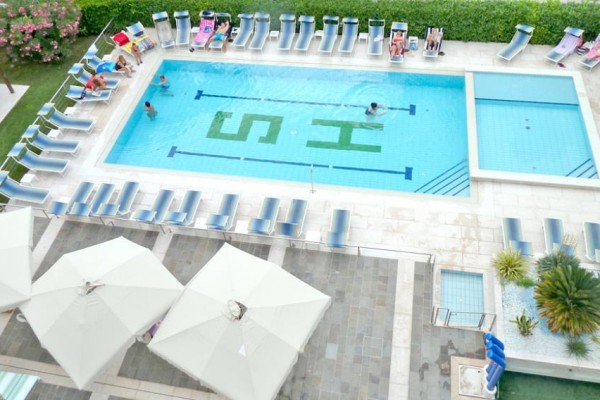 Hotelowy basen otoczony leżakami i parasolami, z kąpiącymi się ludźmi wewnątrz.