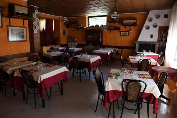 Restauracja z pomarańczowymi ścianami, nakrytymi stołami i drewnianymi krzesłami.