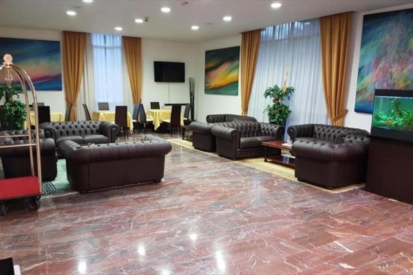 Hol hotelowy z skórzanymi sofami, akwarium i malowanymi obrazami na ścianach.
