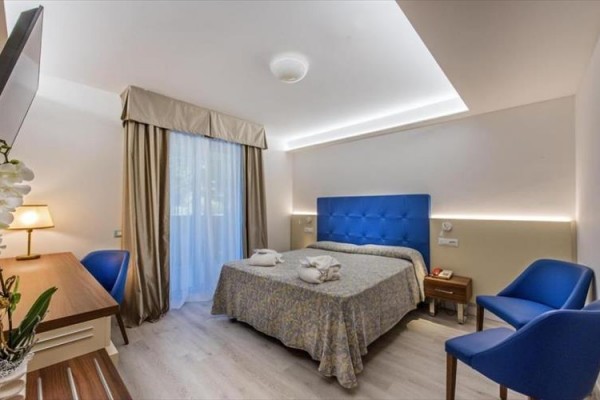 Nowoczesny pokój hotelowy z podwójnym łóżkiem, niebieskimi fotelami i biurkiem.