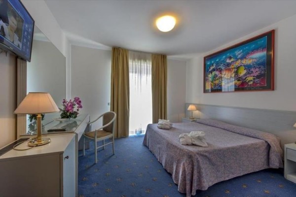 Pokój hotelowy z łóżkiem małżeńskim, telewizorem, biurkiem i obrazem na ścianie.
