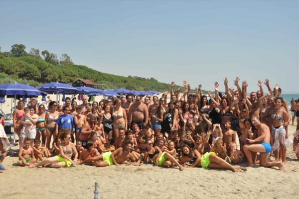 Grupa ludzi bawi się na plaży nad morzem z niebieskimi parasolami w tle.