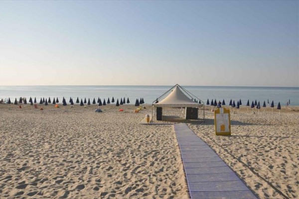 Pusta plaża z rzędem zamkniętych parasoli i altanką na piaszczystym wybrzeżu nad morzem.