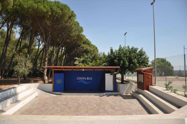 Przestrzeń zewnętrzna z podium i napisem Costa Blu otoczona drzewami.