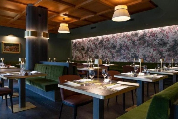 Elegancka restauracja z drewnianym sufitem, kwiatową tapetą i stolikami gotowymi do posiłku.