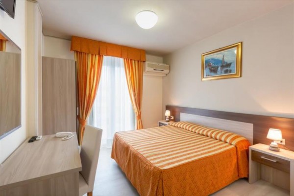 Pokój hotelowy z łóżkiem małżeńskim, zasłonami i klimatyzacją ścienną.