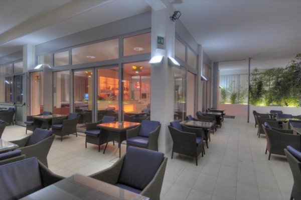 Elegancki zewnętrzny taras restauracyjny z wygodnymi fotelami i stolikami, za szklanymi drzwiami oświetlone wnętrze.