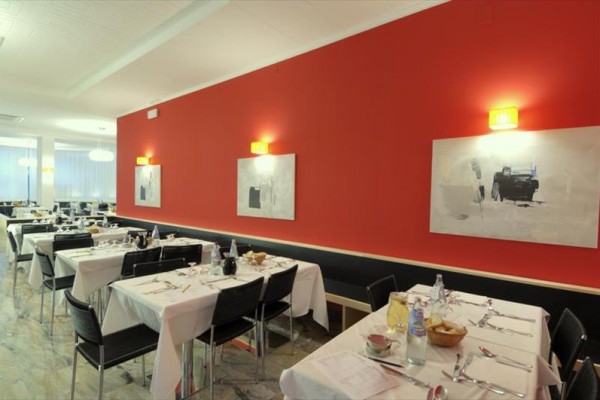 Restauracja z czerwoną ścianą, nakrytymi stołami i nowoczesnymi obrazami.
