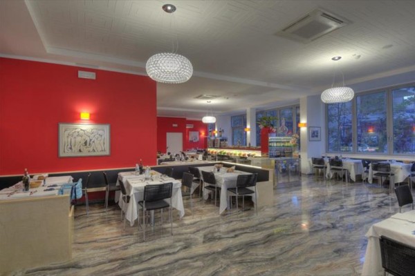 Nowoczesna restauracja z czerwonymi ścianami i eleganckimi żyrandolami nad nakrytymi stołami.