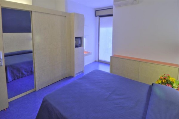 Nowoczesny pokój hotelowy z niebieskim łóżkiem i drewnianymi elementami.