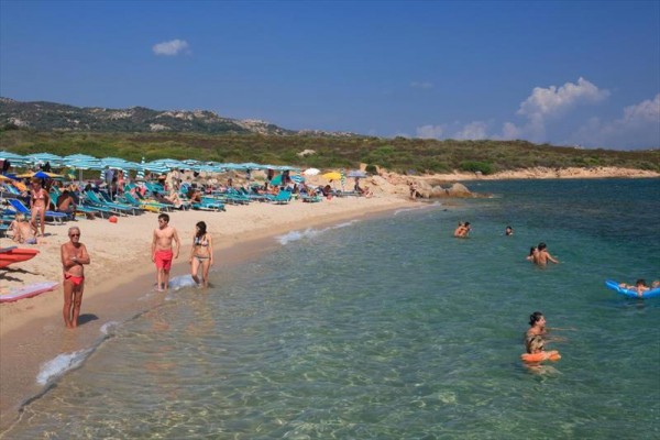 Piaszczysta plaża z ludźmi kąpiącymi się i opalającymi pod parasolami.