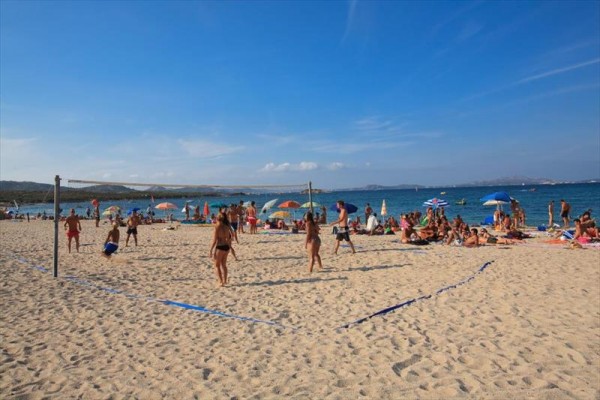 Ludzie grają w siatkówkę plażową blisko kąpiących się na plaży.