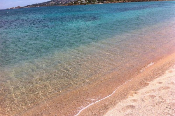 Piaszczysta plaża z przejrzystym błękitnym morzem i odległymi górami.