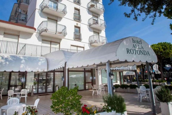 Biały budynek hotelu z tarasem i markizą z napisem 