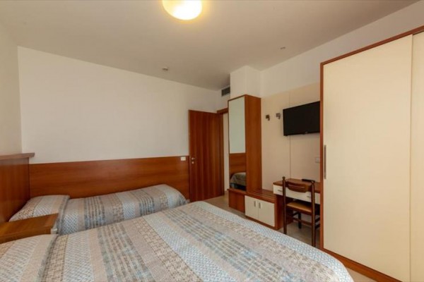 Pokój hotelowy z dwoma łóżkami, szafą i telewizorem na ścianie.