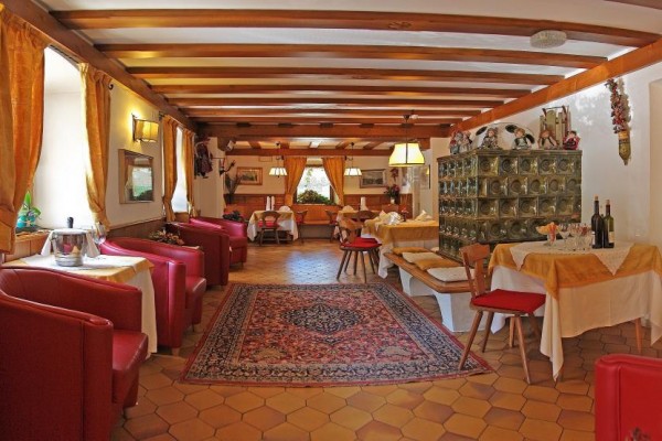 Stylowa restauracja z drewnianymi belkami, dywanami i czerwonymi fotelami.