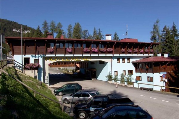 Budynek hotelowy z kwiatami na balkonach i zaparkowanymi samochodami przed nim.