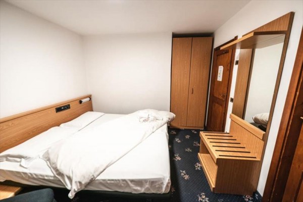Prosty pokój hotelowy z podwójnym łóżkiem, szafą i lustrem.