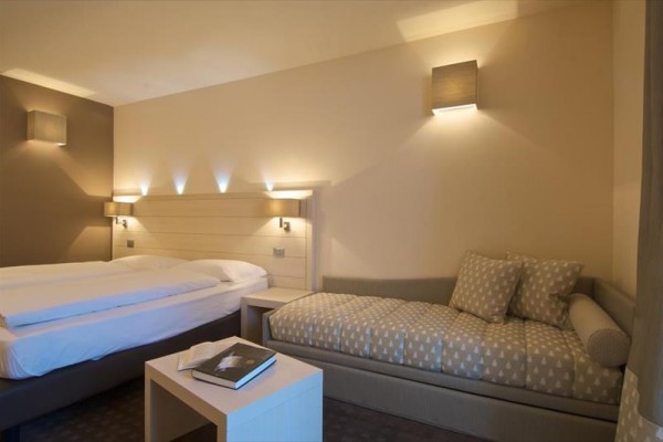 Nowoczesny pokój hotelowy z łóżkiem małżeńskim, sofą i stolikiem z książką.