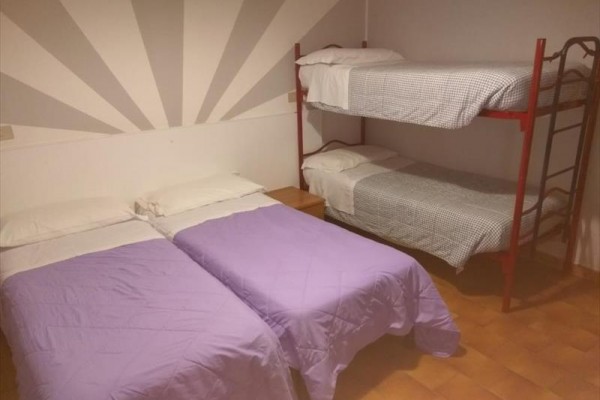 Dwa pojedyncze łóżka z fioletowymi nakryciami i łóżko piętrowe w rogu pokoju z pomarańczową podłogą.