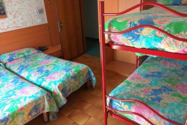 Pokój z łóżkiem piętrowym i dwoma osobnymi łóżkami z kolorową pościelą.