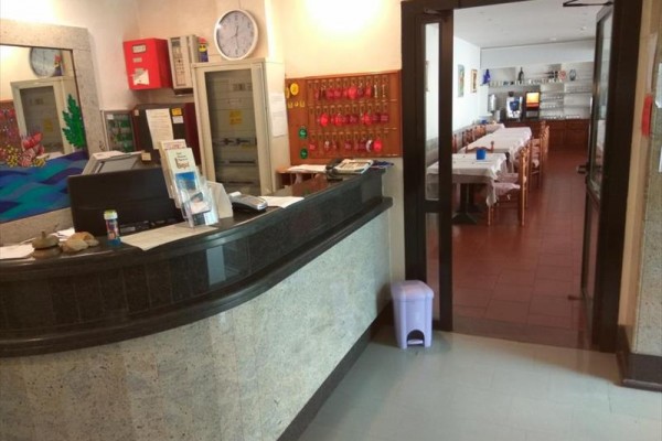 Recepcja z ladą, za którą znajdują się klucze, obok sala z jadalnianymi stołami.