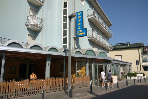 Hotel z niebieską fasadą i balkonami, wejście z napisem 